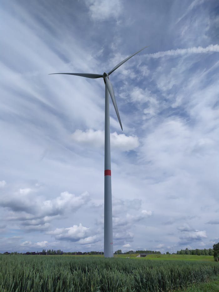 about-header A tall wind turbine stands in a lush field against a dramatic, cloudy sky, symbolizing renewable energy.